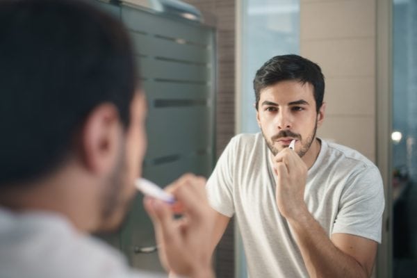 hispanic-man-brushing-teeth-in-bathroom-at-UPDQ4K8-min