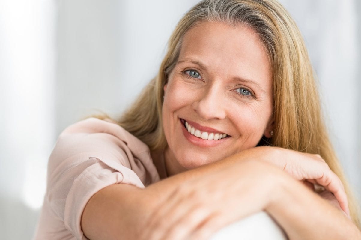 smiling-mature-woman-on-couch-JEHUQVG-min-1204x800
